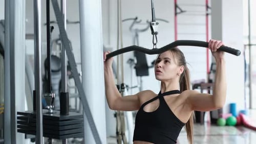 Una mujer entrena los músculos de los brazos y la espalda en el gimnasio