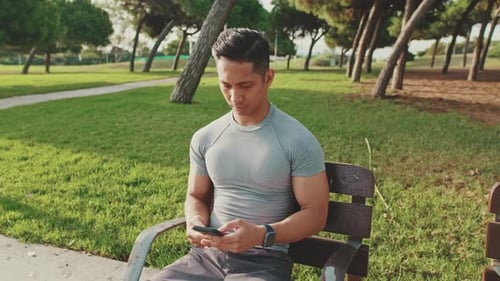 Young man sitting on a park bench uses a mobile phone