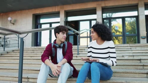 Cheerful multiethnic student friends talking while sitting on the stairs of the university