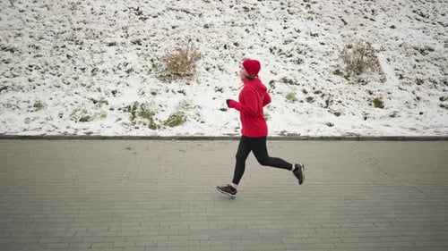 Woman Jogging Outdoors in Winter Next to Snowy Hill