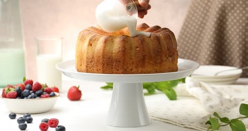 Woman glazing delicious bundt cake at white table, closeup