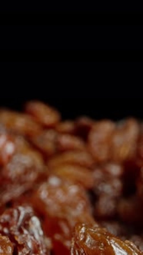 Vídeo vertical. Pasas sobre fondo negro. Un primer plano de una macrofotografía de uvas secas. Pasas negras.