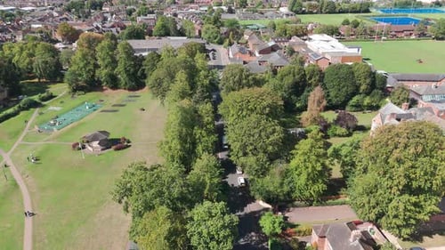 An aerial shot of a park, recreation area, next to a tree-lined, shaded street. In the background