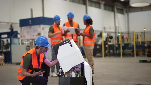 Ein multiethnisches Team von Ingenieuren arbeitet zusammen, wartet und programmiert einen Roboter mithilfe eines digitalen