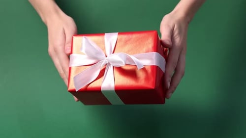 Woman holding gift box against green background, closeup. Merry Christmas and Happy New Year
