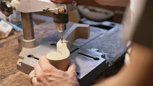 A violin maker prepares the top of a violin by drilling.