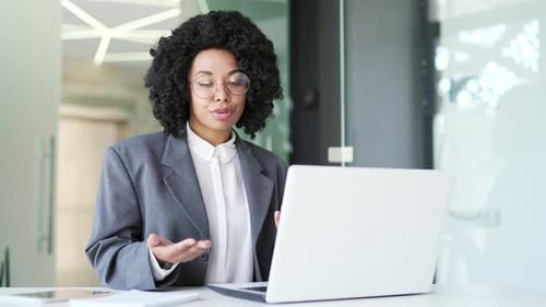 Woman in Blazer Talking Into Laptop in Office