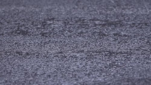 Regen fällt auf Asphalt und erzeugt kleine Pfützen