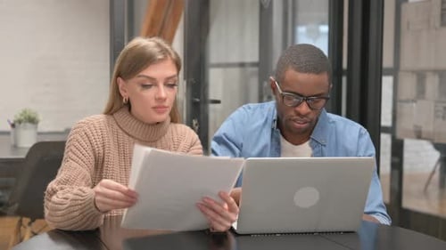 Adults Discussing Documents at Desk with Laptop