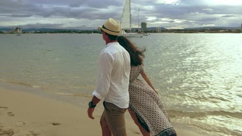 Beautiful Young Caucasian Couple Walking on the Beach, Holding Hands Under A