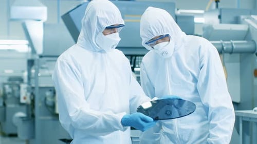 Two Engineers/ Scientists/ Technicians in Sterile Suits Hold Semiconductor Silicon Wafer That Will