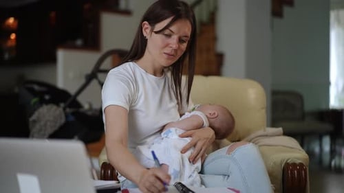 Young Mother Multitasking Holding a Sleeping Baby While Working From Home