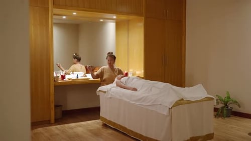 Senior Biracial Masseuse Does Facial Massage with a Jade Roller to Female Client at Spa Center Adult