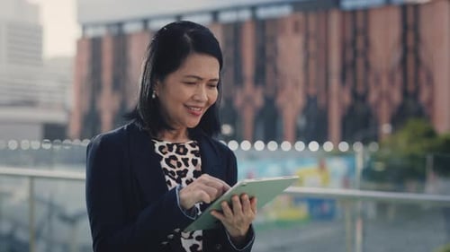 Positive Asian Lady Using Tablet Texting with Clients Charming Smiling Senior Female Boss Chatting