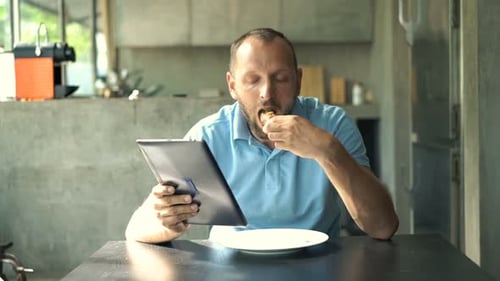 Man uses tablet while eating in modern kitchen