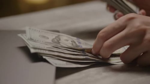 Hands Counting Money Next to Laptop