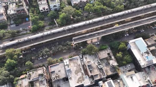 Top-down aerial view of a Delhi Metro train gliding along elevated tracks above dense residential