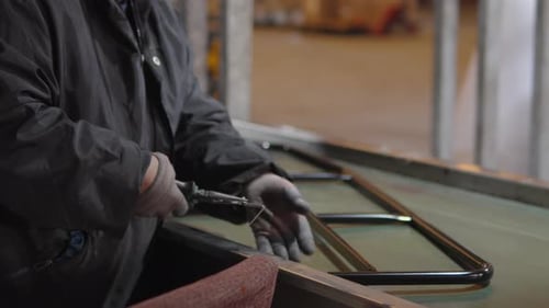 Factory Worker in Dark Coveralls and Gloves Carefully Assembling Numerous Metal Window or Door
