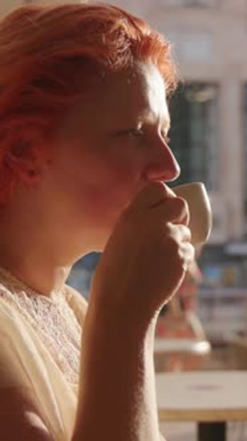 A Woman Who is Enjoying a Warm Cup of Coffee While Watching the Sunset Glow in a Cozy Cafe