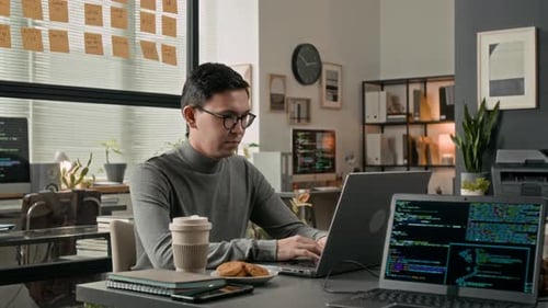 Young System Administrator Working on Laptop at Wooden Desk in Modern Office