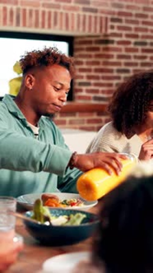 Young Man Pours Juice for Family During Meal