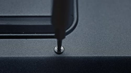 Screwdriver Tightening Screw in Black Metal Surface