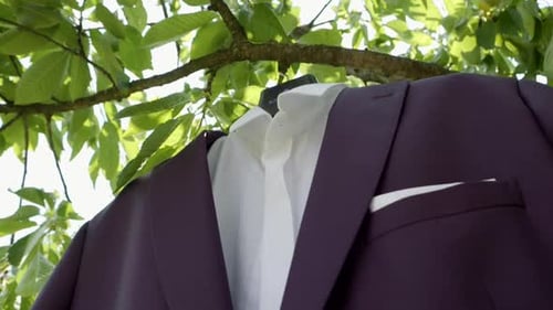 A fragment of the groom's jacket and shirt hanging in a garden