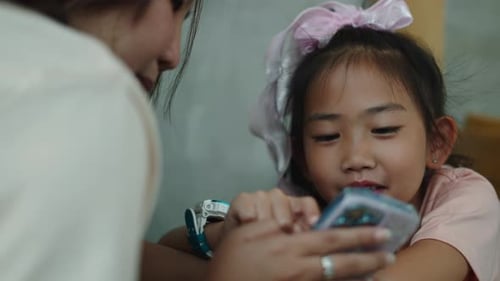 Child and Adult Watching Smartphone Device Together Indoors