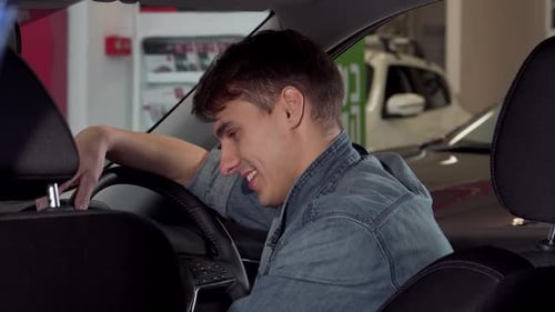 Joyful Man Giving a Thumbs Up While Seated in a Sleek New Car at the Dealership