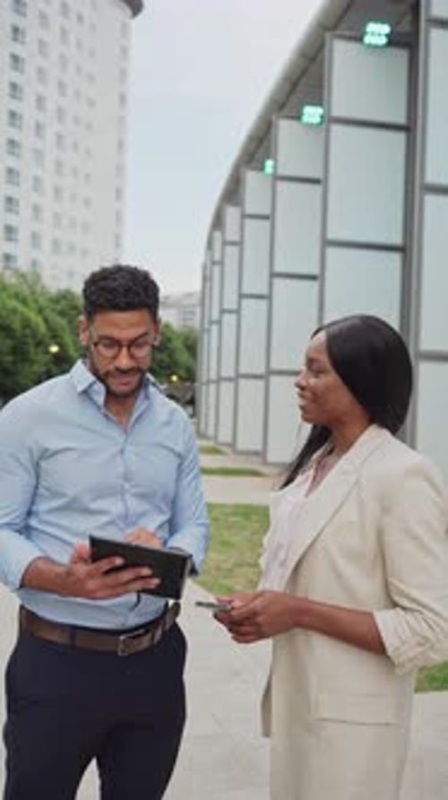 two diverse smiling Business colleagues discussing work on tablet outside office