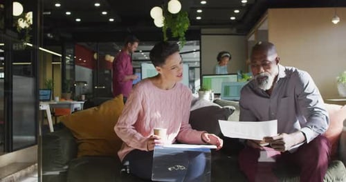 Diverse business people sitting with documents and discussing work at office