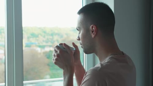 Man Drinking from Mug Looking Out Window