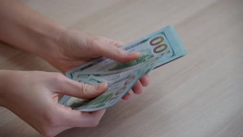 Close-up of a woman's hands counting a stack of dollars on a wooden table