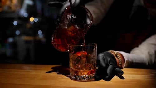 Bartender pouring drink from a glass bottle into glass with ice ready to serve final drink close-up