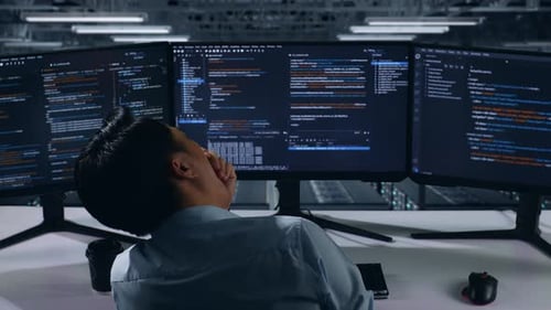 Rückansicht eines müden asiatischen Entwicklers, der beim Schreiben von Code im Rechenzentrum gähnt