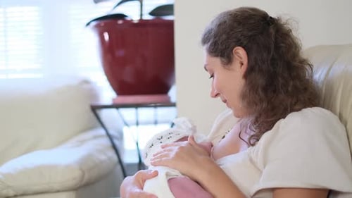 Mother Gently Nursing Newborn Baby Indoors in Daytime