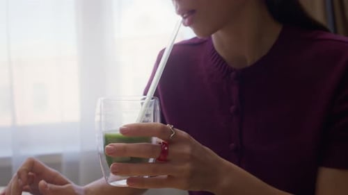 Young Adult Woman Drinks Green Smoothie While Using Laptop