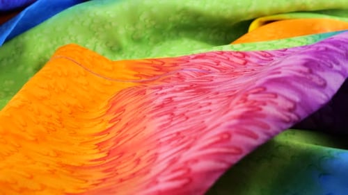 Close-up view of a shirt made of bright fabric dyed in rainbow colors rotates on a display case.