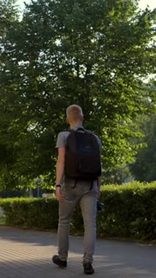 Vertical of Young Photographer is Walking Along a City Street Behind Him