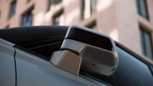 Automatic Folding Out Mirror of a Gray Car in a City Parking Lot Among Modern Buildings The Mirror