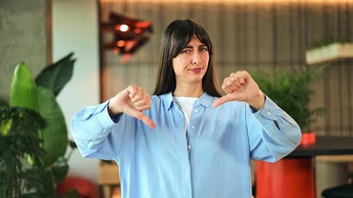 Young Woman Expresses Disapproval with Thumbs Down Gesture in Modern Office