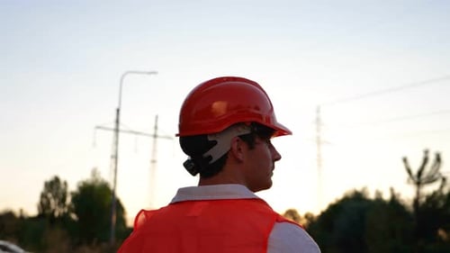 Worker in Hard Hat near Power Lines at Sunset
