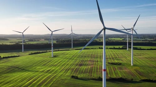 Aerial footage of a wind farm with large spinning wind turbines. The camera is flying backward over