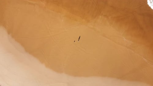 Drone aerial spin pan shot of ocean sea shoreline landscape with waves tide crashing on sandy beach