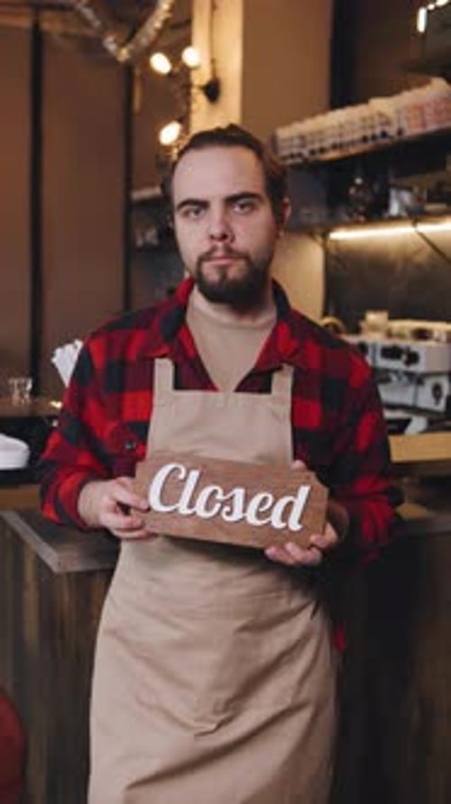 Barista Holding Closed Sign in Cafe with Coffee Tools and Roasting Equipment Visible in Background