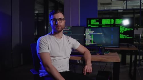 Portrait Of Programmer In Dark IT Office Sitting At Desk