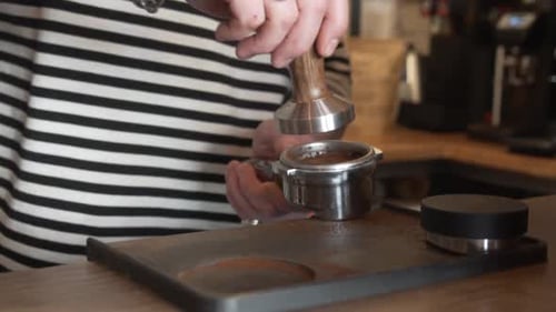 Professional Barista Using A Tamper To Press Ground Coffee In Portafilter. close up, slow motion