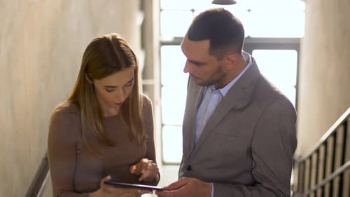 Man and Woman Discussing a Tablet in Stairwell