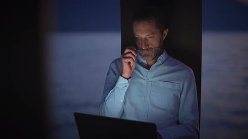 Un homme concentré travaille tard sur son ordinateur portable au bord de l'eau paisible au coucher du soleil