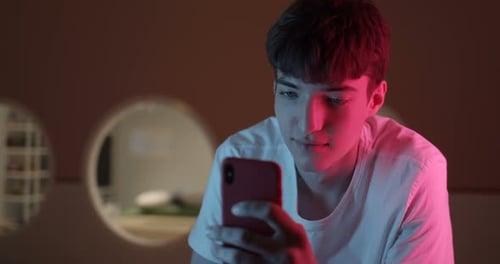 Teenage Boy Using a Mobile Phone Indoors at Night